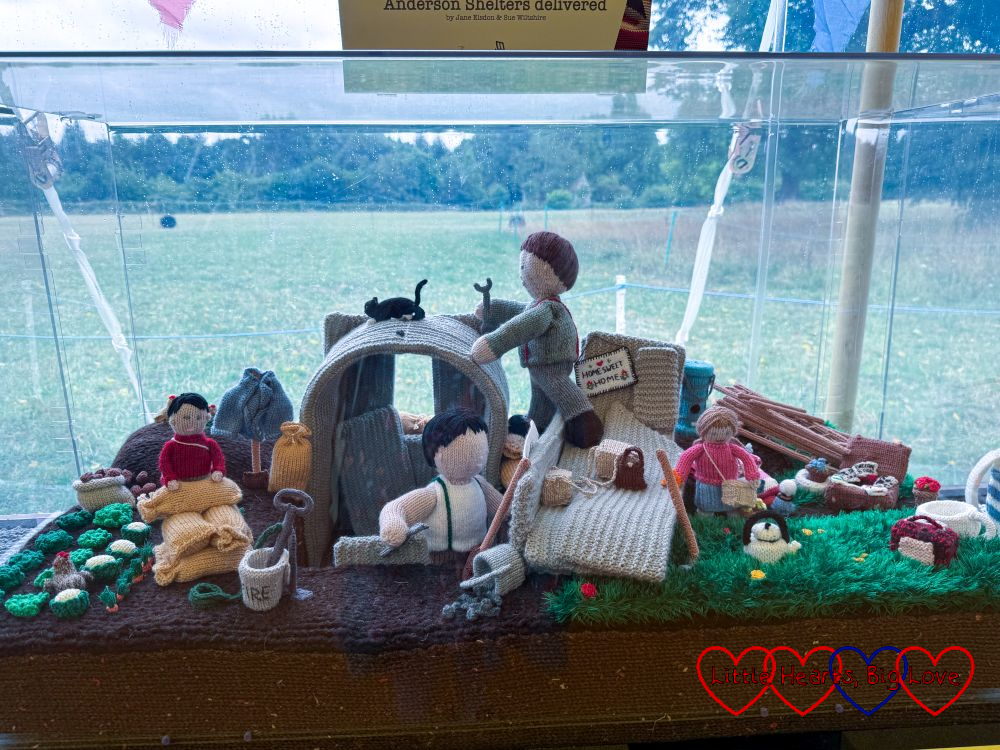 A knitted scene showing an Andersen shelter being built in a back garden