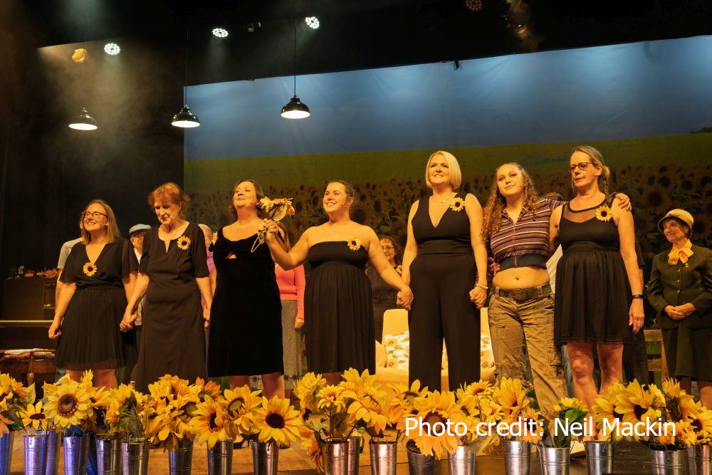 A photo from the dress rehearsal of Calendar Girls showing the girls wearing black dresses with sunflower pins