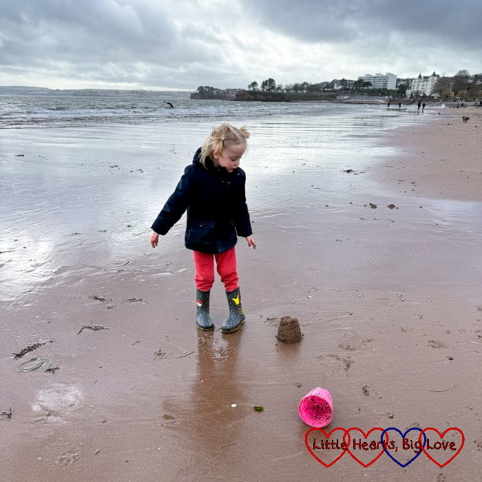 Thomas standing next to a sandcastle on the beach