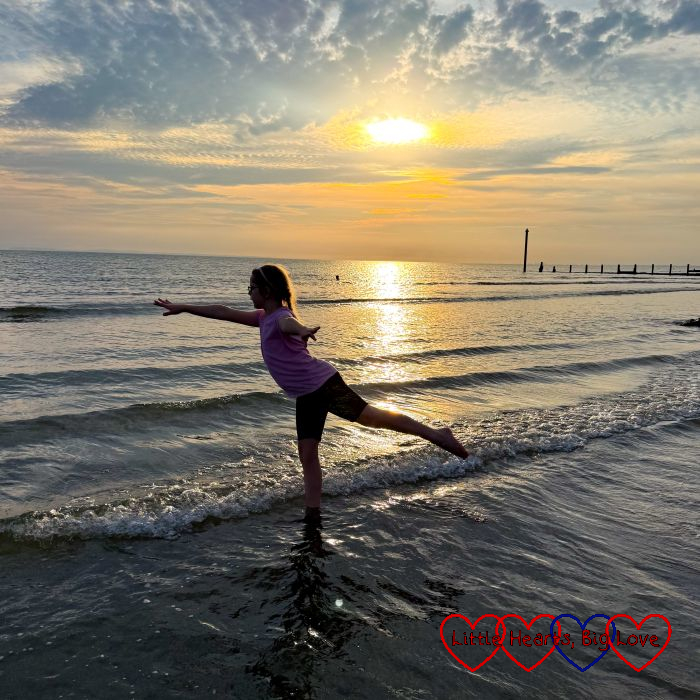 Sophie in arabesque pose on the beach against a sunset sky