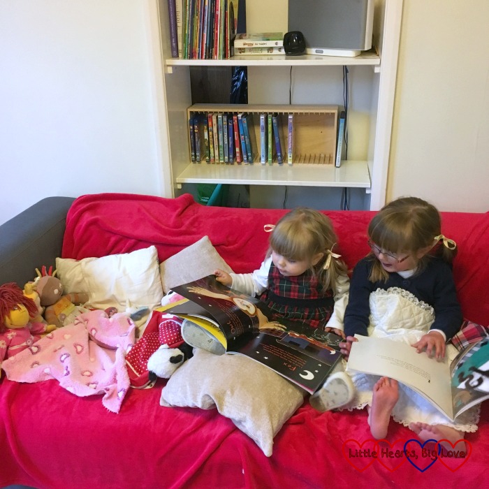 The girls itting on the sofa and reading a bedtime story to their toys