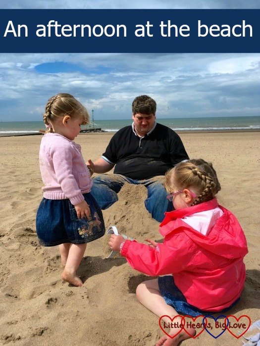 My two girls at the beach trying to build a sandcastle whilst burying Daddy with the text "An afternoon at the beach"