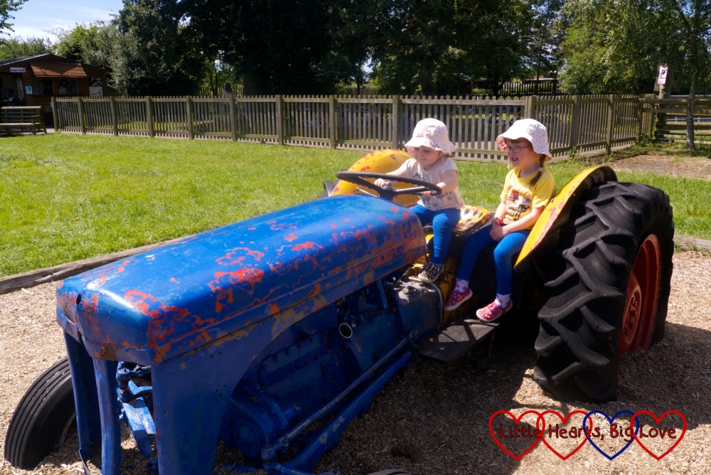 Jessica and Sophie driving a blue tractor in the play area at Odds Farm Park