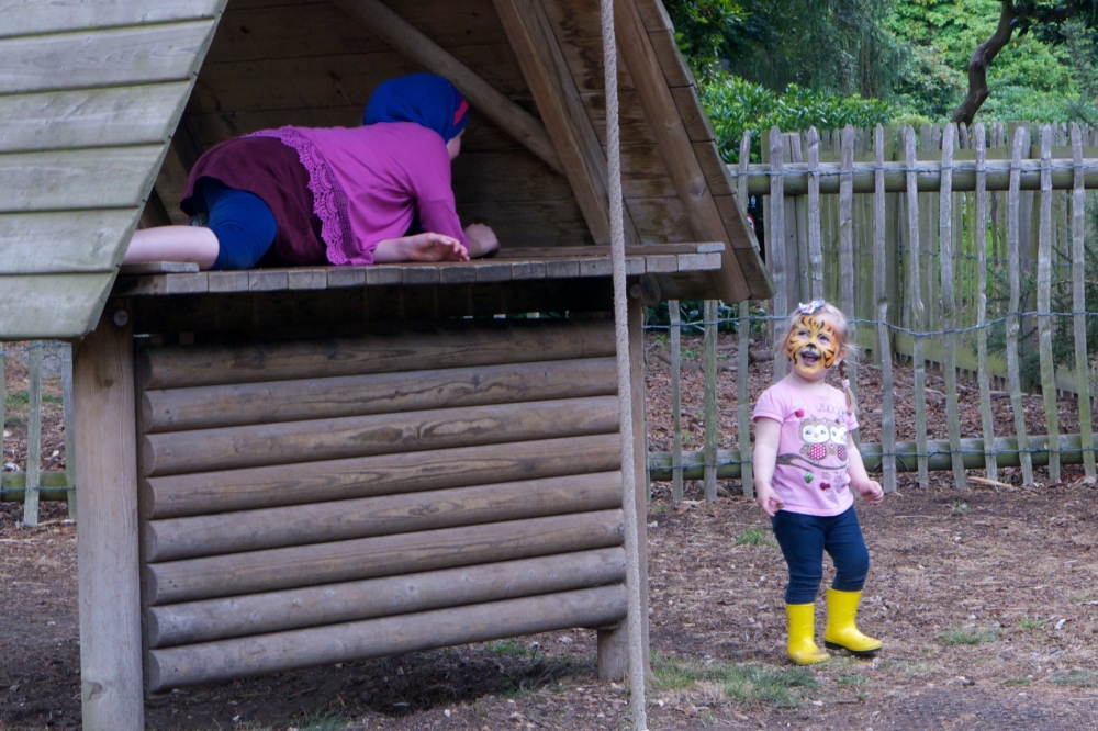 A tiger-faced Sophie prowling around the huts in the playgruond while an older girl hides from her