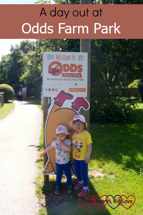 Jessica and Sophie standing in front of one of the signs at the entrance to Odds Farm Park with the text "A day out at Odds Farm Park"