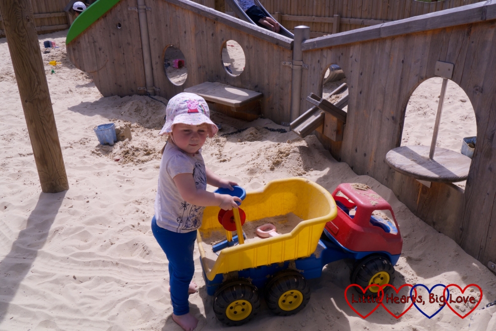 Sophie playing with a dumper truck in the sandy area