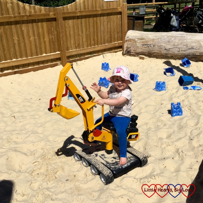 Sophie riding a mini digger in the sandy area