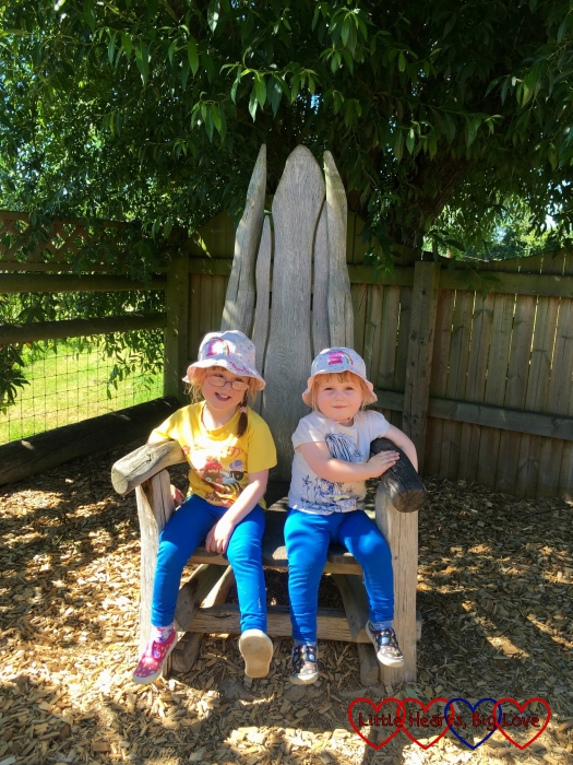 Jessica and Sophie sitting together in a big wooden chair in one of the play areas at Odds Farm Park