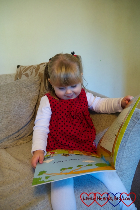 Sophie sitting on the sofa "reading" the Harty Hedgehog and his BuZZy Friends book