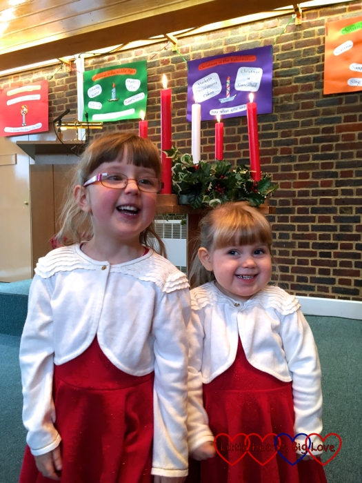 Jessica and Sophie in their Christmas dresses standing in front of the Advent candles at church