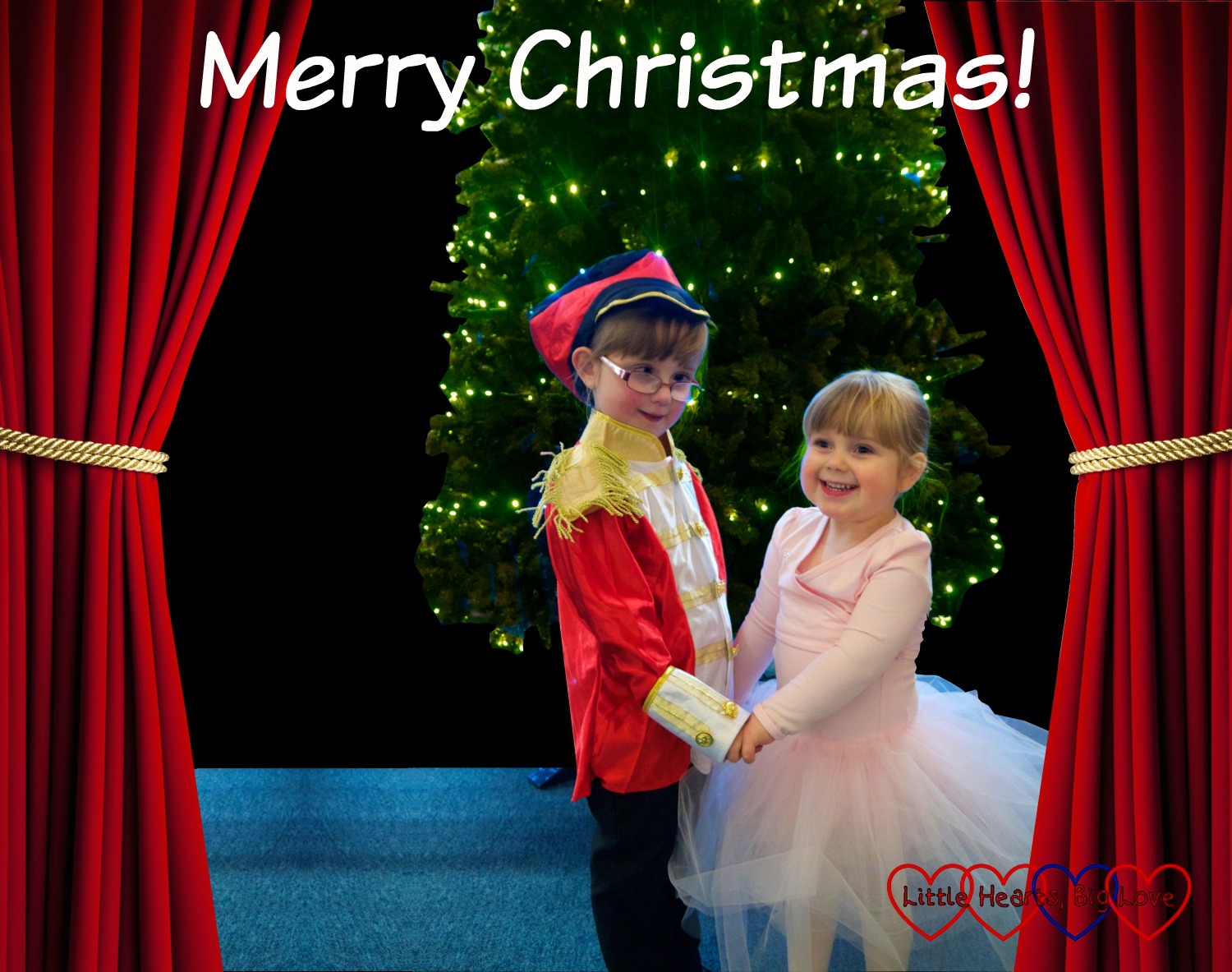 Jessica dressed in a soldier costume and Sophie in a pink tutu standing in front of a Christmas tree with stage curtains either side of them and the text "Merry Christmas"