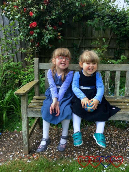Jessica and Sophie sitting on a bench wearing their reversible dresses from Seesaw children's clothes