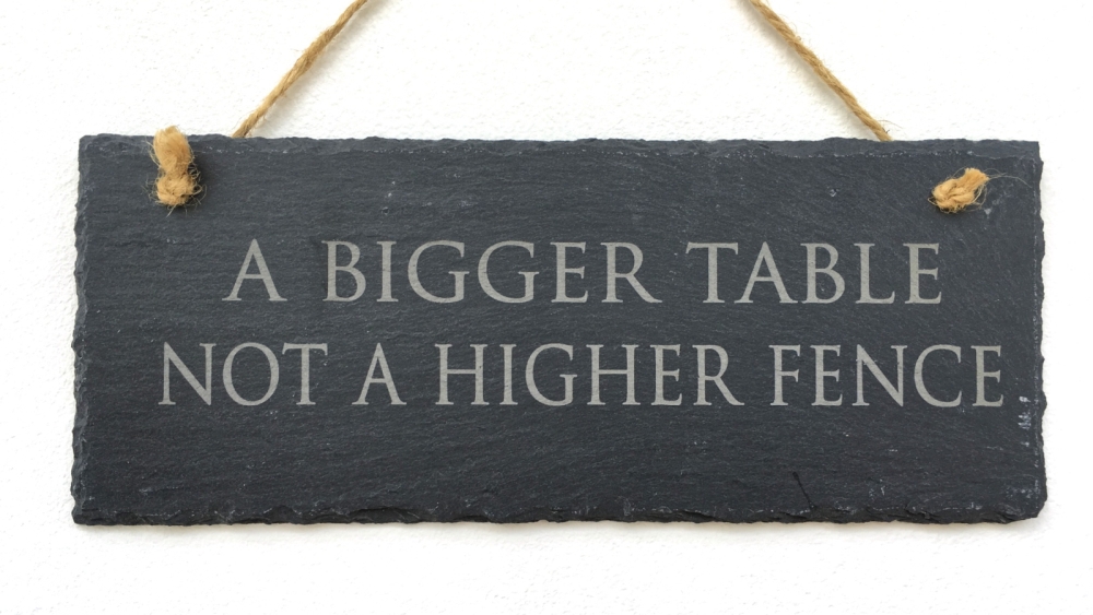 A sign with the quote "A bigger table, not a higher fence"