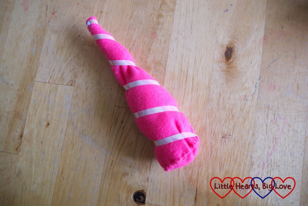 A unicorn horn made from a cone of pink felt with ribbon wound around it