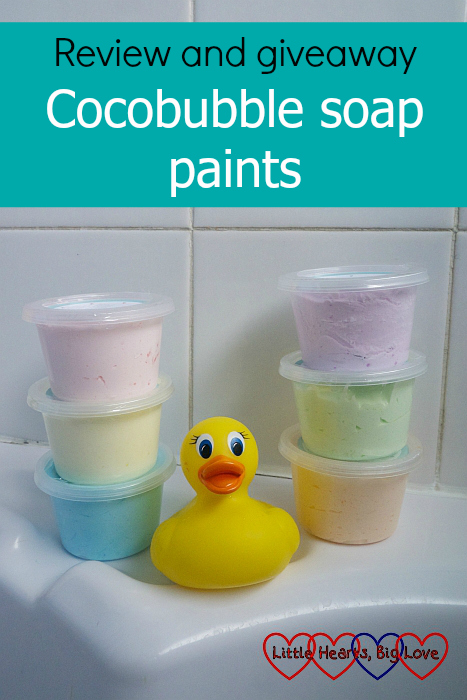 Six Cocobubble soap paint pots in pink, yellow, blue, purple, green and orange on the edge of a bath tub with a yellow duck sitting in the middle - "Review and giveaway: Cocobubble soap paints"