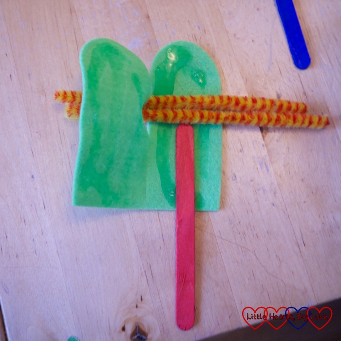 Two pieces of felt partly joined with a craft stick glued on one and pipe cleaners across the middle