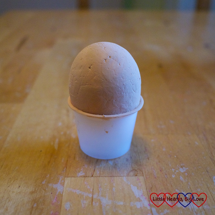 A polystyrene egg painted with skin-coloured paint, sitting in a small plastic pot 