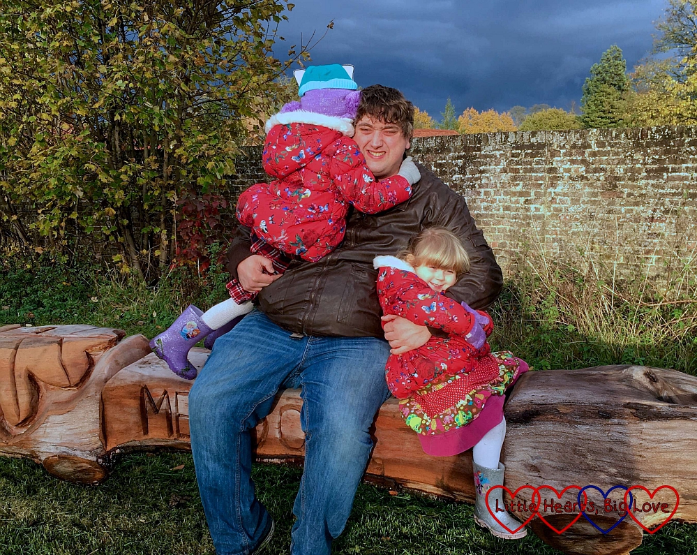 Hubby sitting on a bench in the meadow having cuddles with our girls 