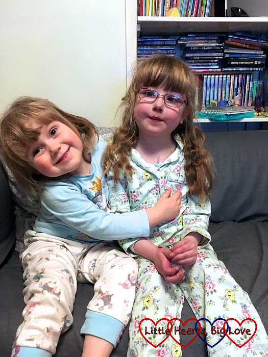 Jessica and Sophie sitting together on the sofa in their pyjamas with Sophie giving Jessica a hug