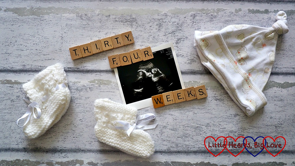 A scan photo with letters spelling "thirty four weeks" plus a baby hat and baby boottees
