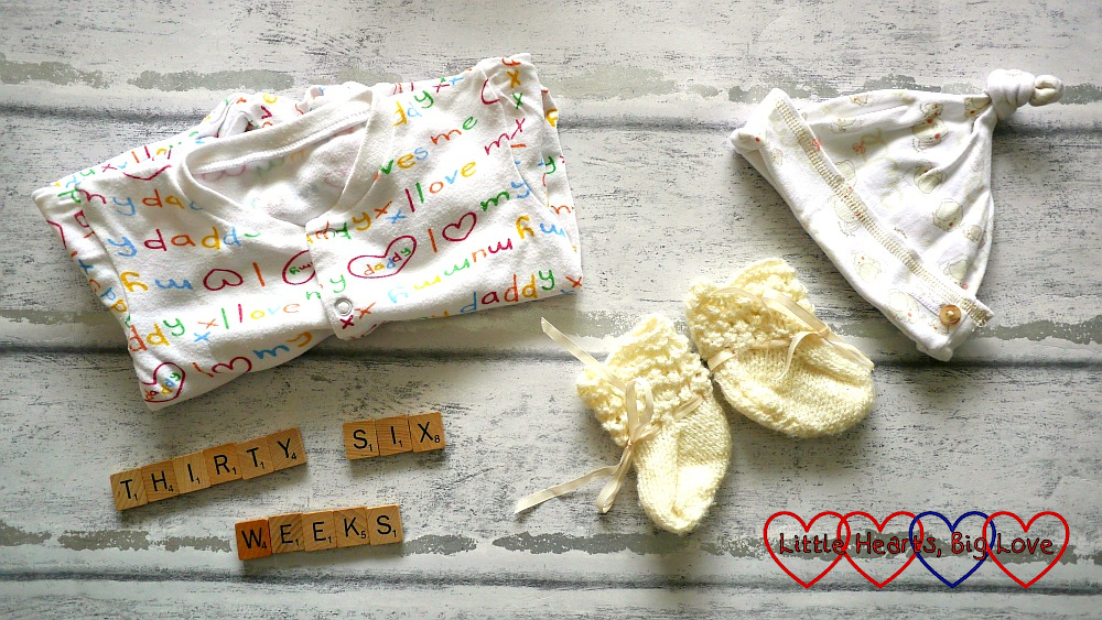A babygro, hat, bootees and Scrabble letters spelling out "thirty six weeks"