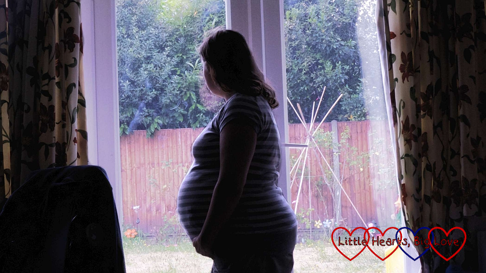 A silhouette of a pregnant woman gazing out of a window