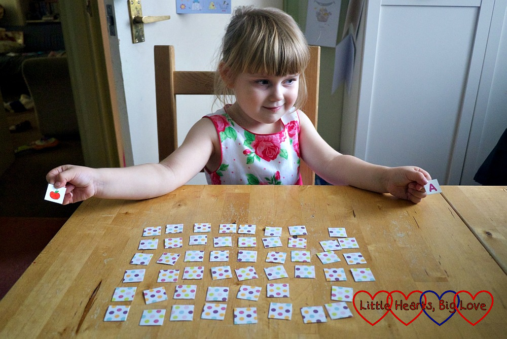 Sophie holding an "A" square and an apple picture square with the rest face down on the table