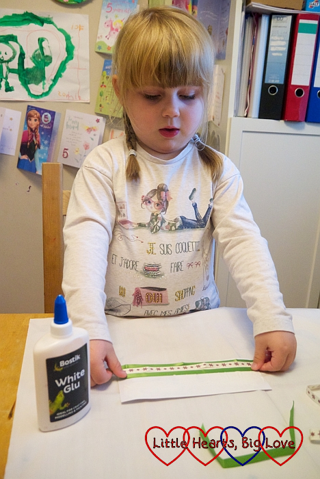Sophie gluing horizontal strips of ribbon to a piece of card