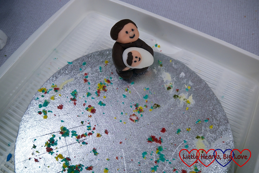 The icing figure of the vicar holding the baby surrounded by rainbow coloured crumbs