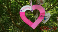 A pink and white heart with "Jessica" written on it hanging in a tree