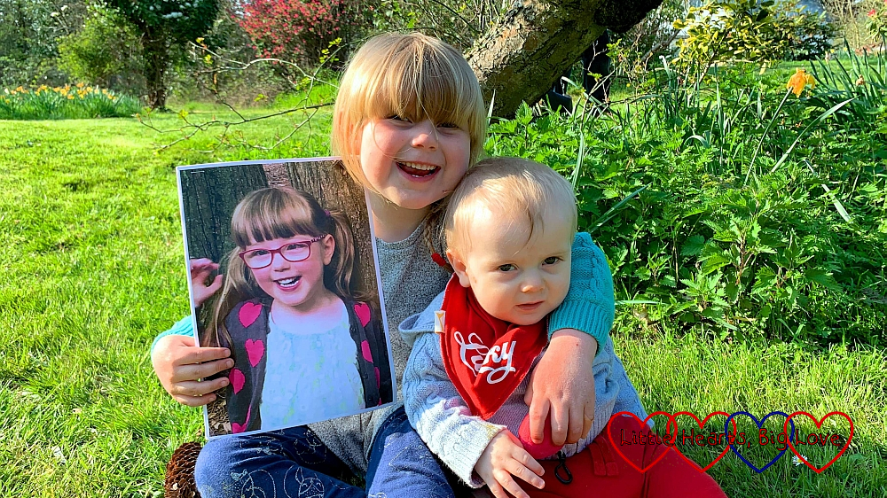 Sophie and Thomas sitting in Grandma's garden, with Sophie holding the picture of Jessica