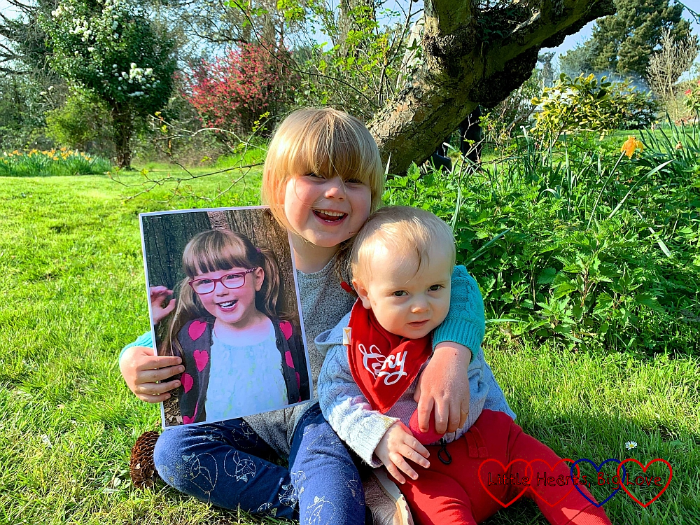 Sophie and Thomas sitting in Grandma's garden, with Sophie holding the picture of Jessica
