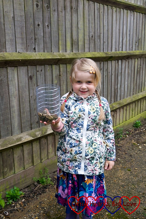 Sophie holding the bottle half of a plastic bottle with a layer of pebbles in the bottom