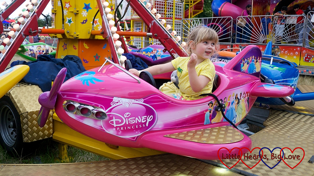 Sophie riding in a pink aeroplane at the fun fair