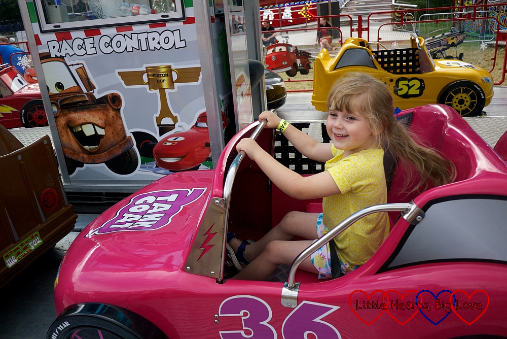 Sophie riding in a pink car at the fun fair