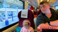 Sophie sitting on the train with her headphones on while hubby looks out of the window at Exeter St David station