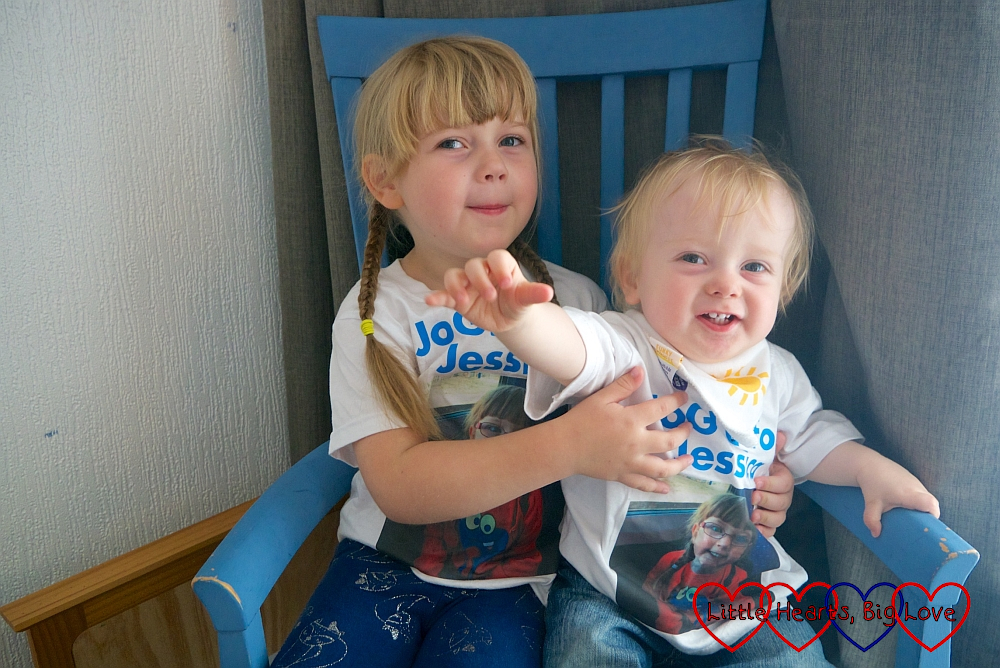 Sophie and Thomas sitting in a blue chair wearing their "JoGLE for Jessica" T-shirts