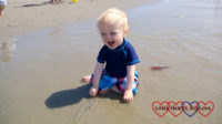 A smiley Thomas splashing in a shallow pool on the beach