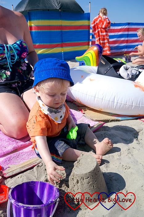 Thomas sitting on the sand and patting the top of a sand castle
