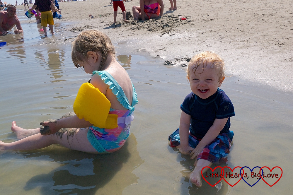 Sophie and Thomas sitting in a shallow pool on West Wittering beach