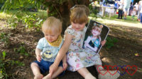 Sophie and Thomas sitting under a tree at Pinner Village Show. Sophie is holding a picture of Jessica