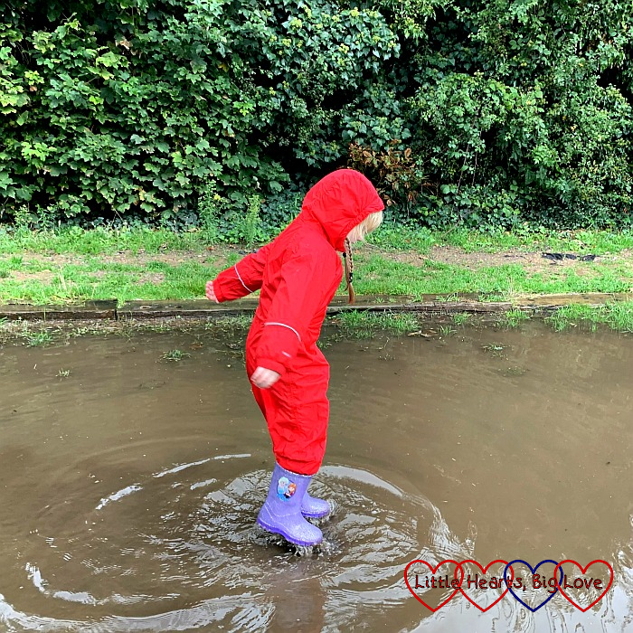 Sophie wearing a red puddle suit and jumping into a big puddle