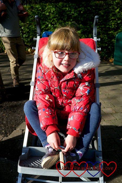 A smiley Jessica sitting in her buggy wearing a red coat