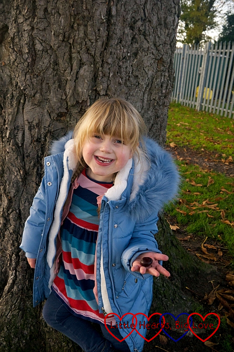 Sophie standing in front of a tree holding a conker in her hand