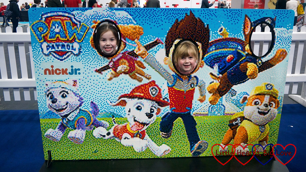 Sophie and her friend popping their heads through the holes in the PAW Patrol mosaic brick board.