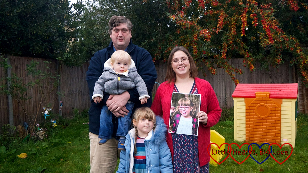 Hubby holding Thomas, me holding a photo of Jessica and Sophie standing in front of us as we pose in the garden