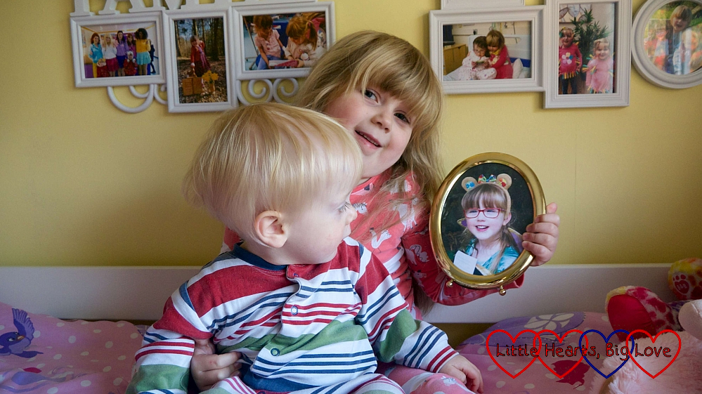 Sophie sitting on her bed, with Thomas on her lap who is looking at a photo of Jessica