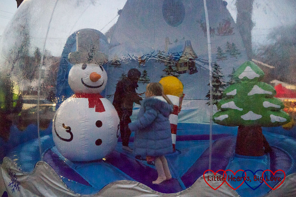 Sophie bouncing around a Christmas tree and snowman inside the inflatable snow globe