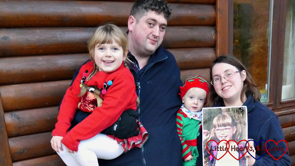 Hubby holding Sophie (wearing a reindeer Christmas jumper) and me holding Thomas (dressed as an elf) and a photo of Jessica outside Heligan Lodge at Coombe Mill