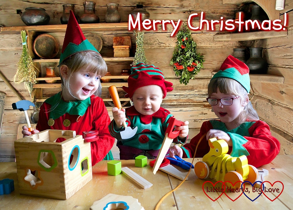 Sophie, Thomas and Jessica dressed as Christmas elves at the table together with a log cabin background with the text "Merry Christmas" across the photo